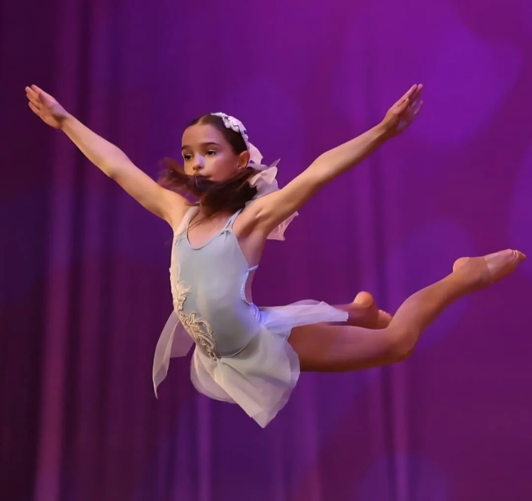 A dancer leaping across the stage under purple lighting, arms outstretched