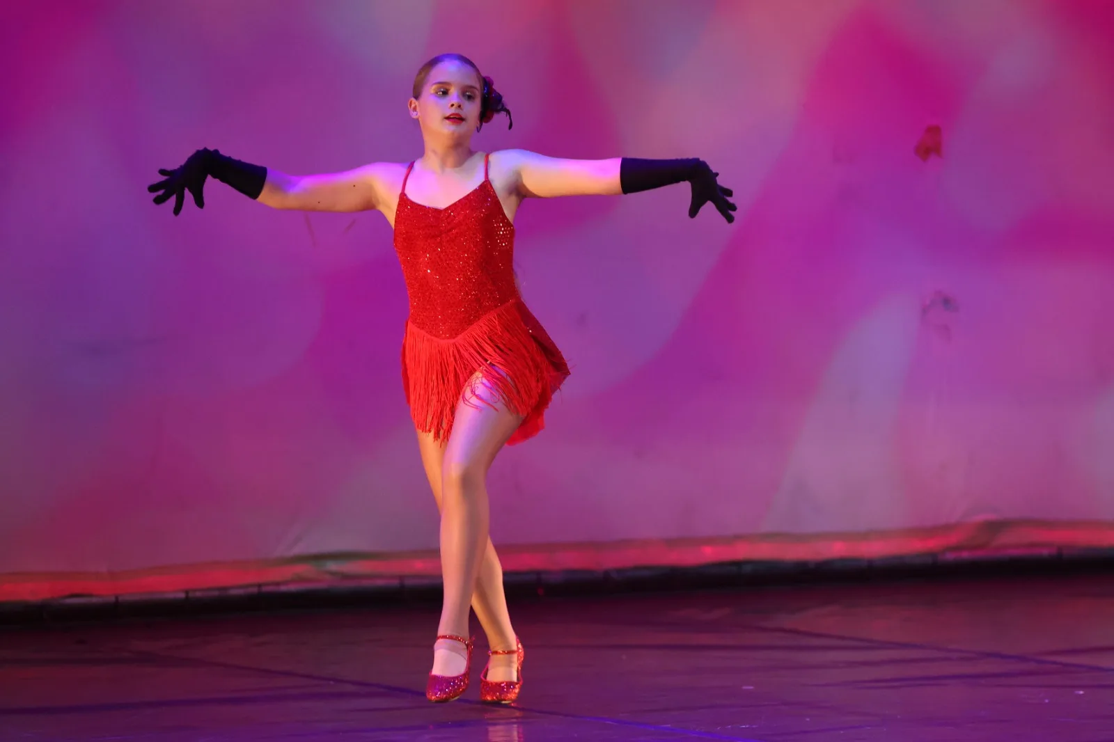 A dancer in a red sequinned fringe dress performing a jazz solo under red stage light