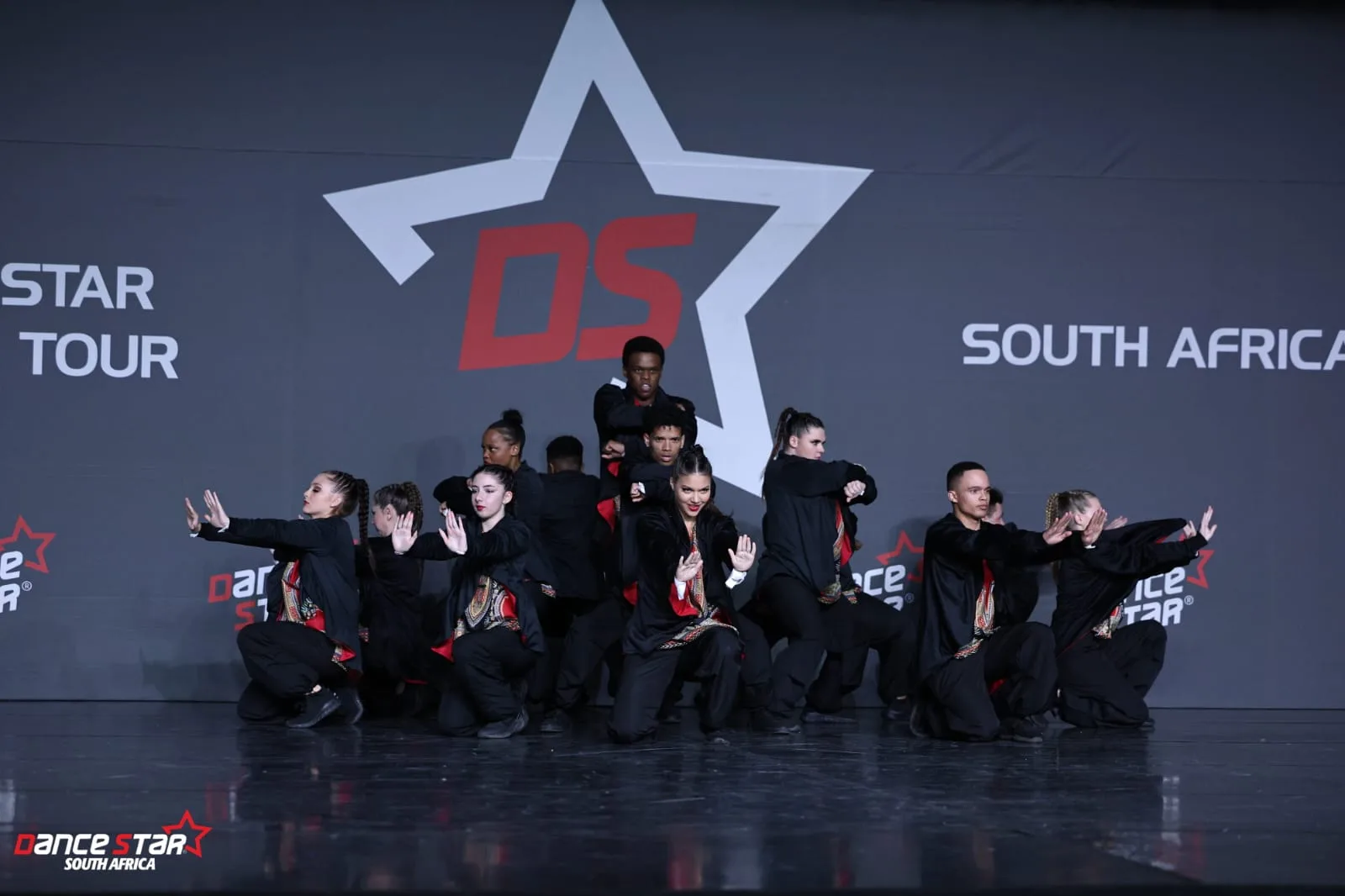 JJDC hip hop dancers kneeling in formation with arms extended at the Dance Star South Africa tour