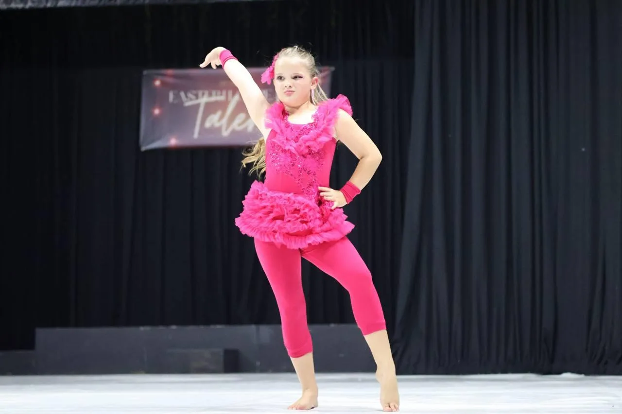 A dancer in a pink ruffled jazz costume striking a pose on stage