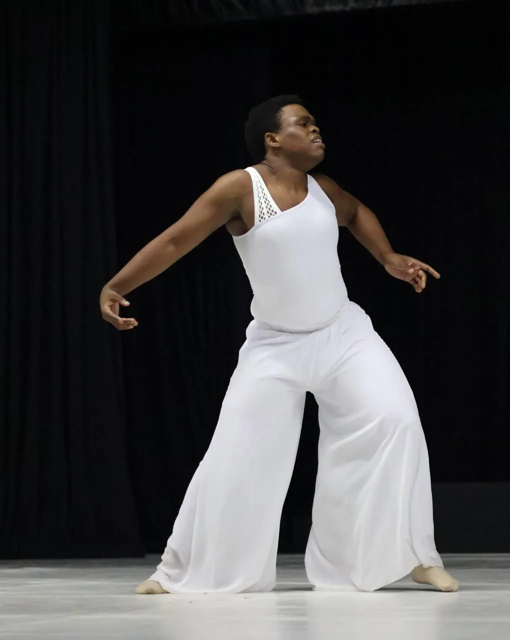 A dancer in a flowing white contemporary costume caught mid-movement against a dark stage