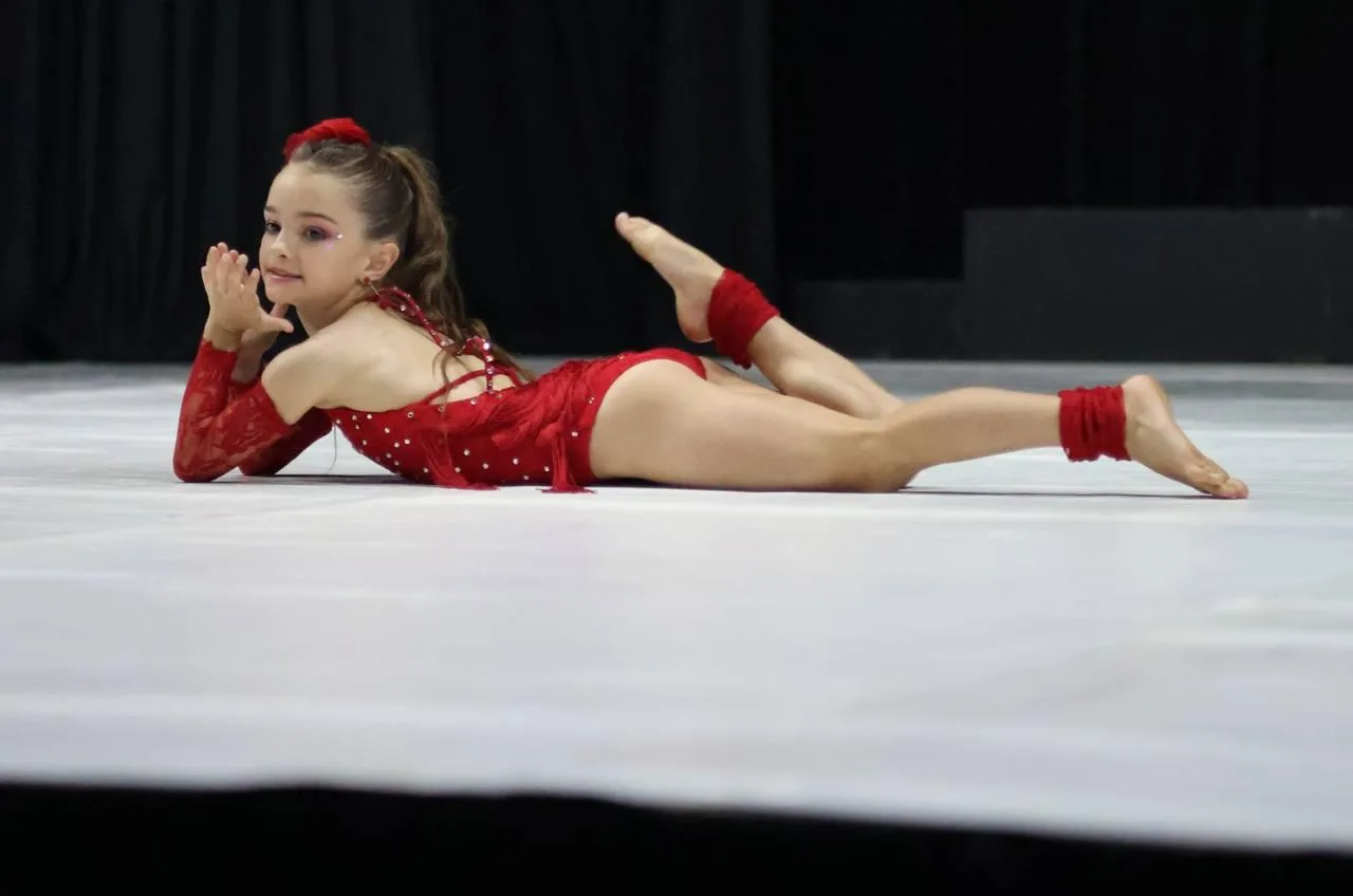 A dancer in red performing a floor sequence during a jazz solo, smiling toward the camera