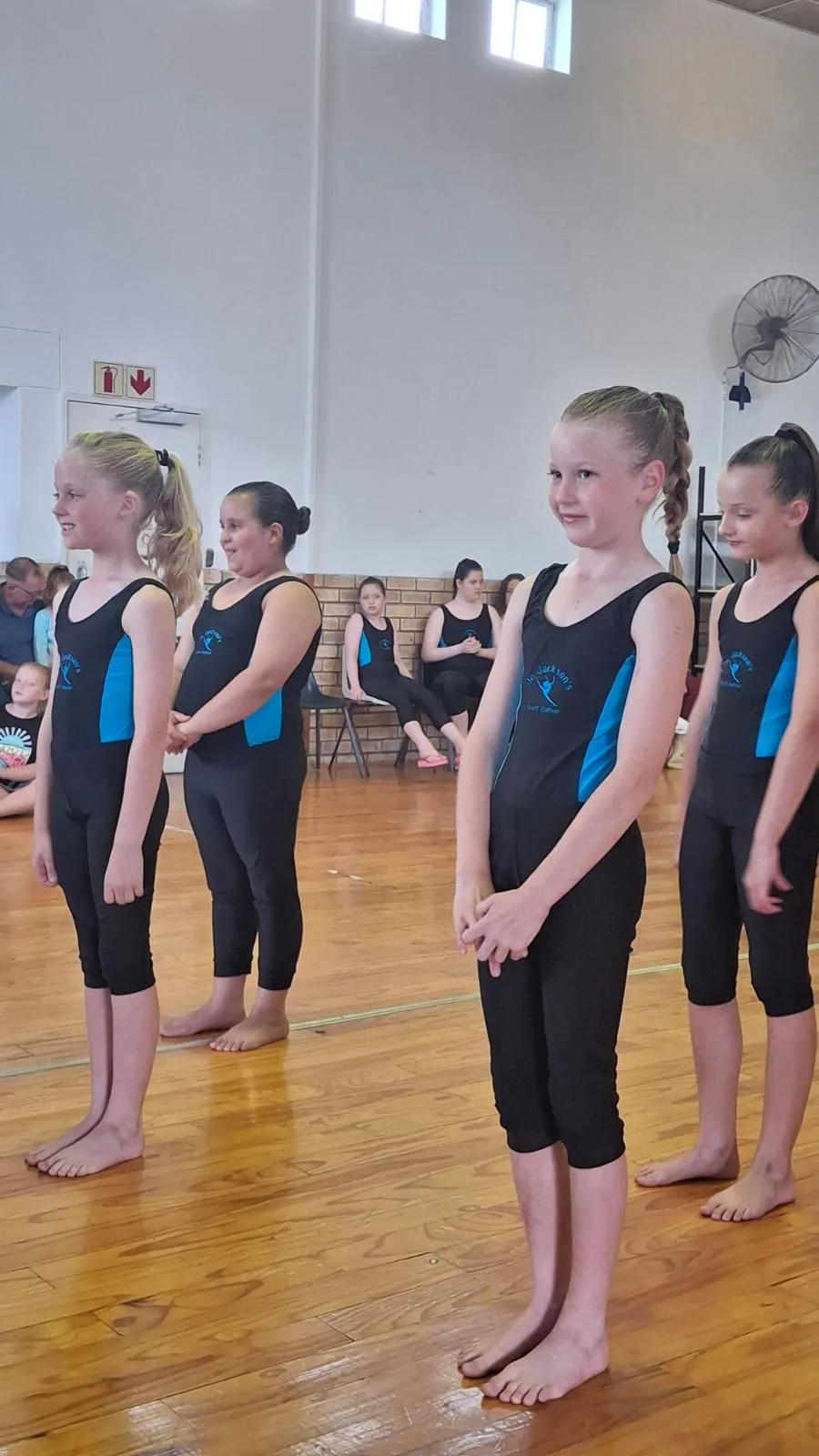 Four young JJDC dancers in black and blue leotards standing in line during a studio session