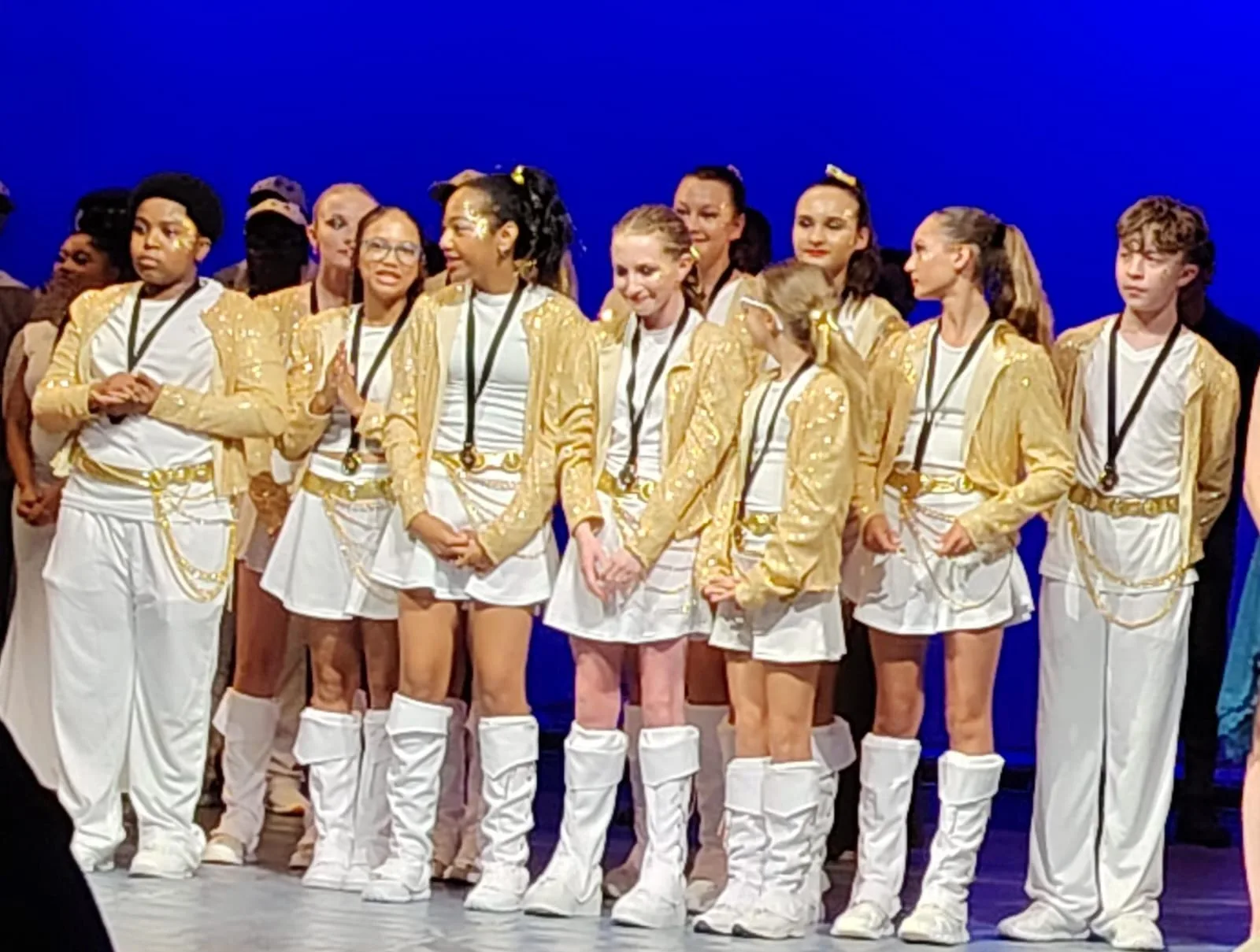 JJDC dancers in gold and white costumes lined up on stage after a performance
